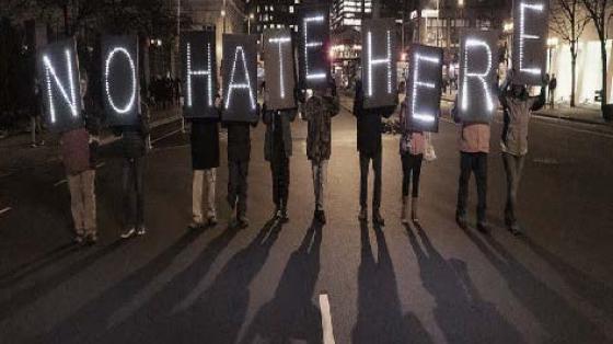 Protestors in the middle of a street, holding a sign that reads "No Hate Here"